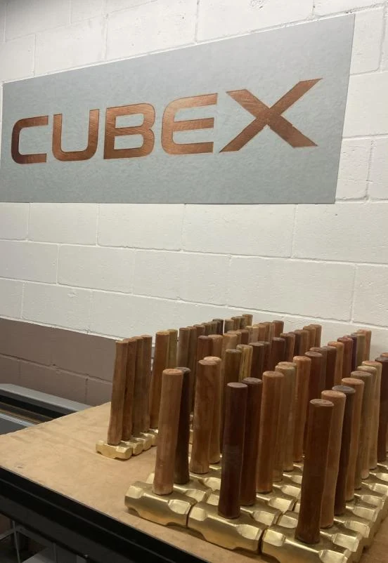Letreiro CUBEX na parede da fábrica, com marretas de bronze montadas sobre a bancada.